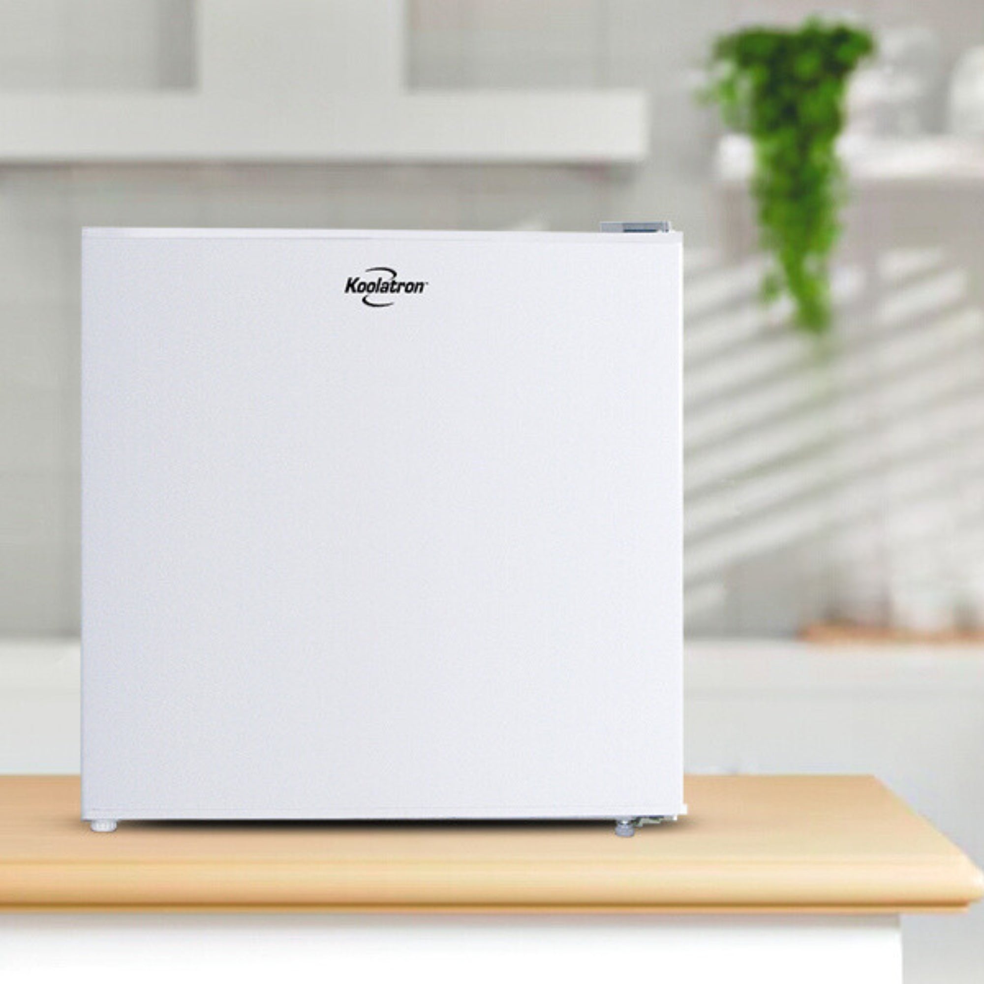 White compact fridge with freezer on a light wooden countertop in a bright white kitchen