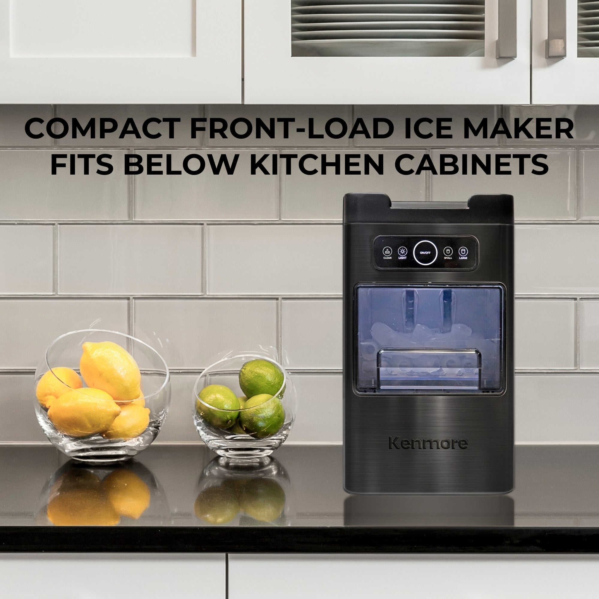 Kenmore space-saving front-load ice machine and glass bowls of lemons and limes on a black kitchen counter with a white tile backsplash and white cabinets above and below. Text overlay reads, "Compact front-load ice maker fits below kitchen cupboards"